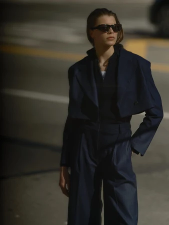Model in dark sunglasses wearing a dark navy blazer and matching trousers outdoors on a city street.