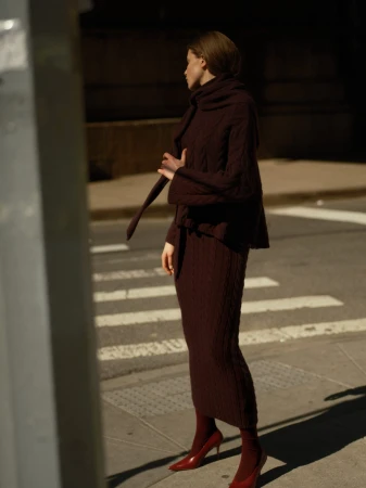 Model standing on a city street wearing a dark knit sweater and matching skirt with red heels