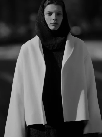 Model wearing a white coat and dark hooded top outdoors in New York City for the Soft Goat Fall 2024 campaign.