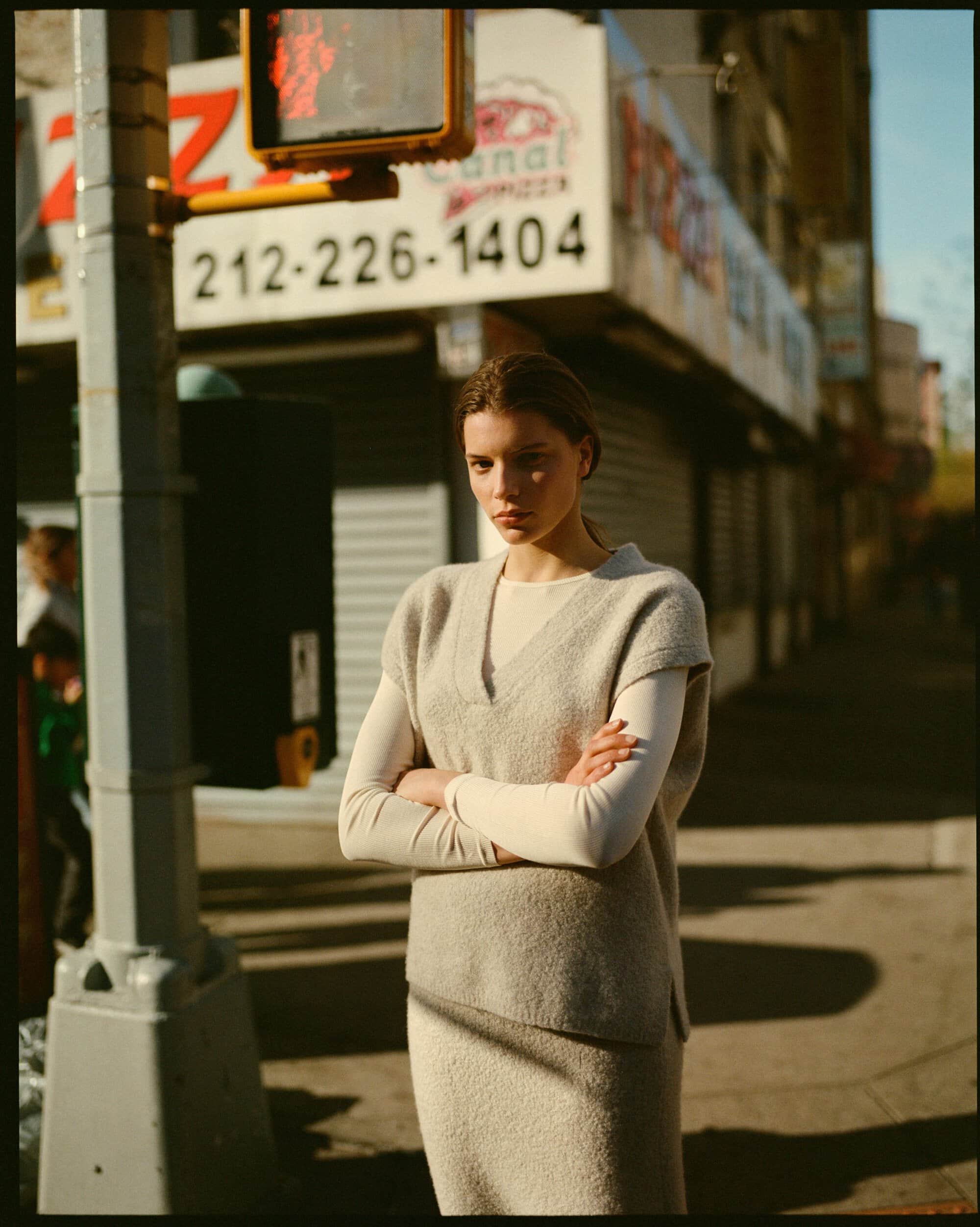 Woman with arms crossed standing on a city street beside a traffic light for Soft Goat Fall 2024 campaign