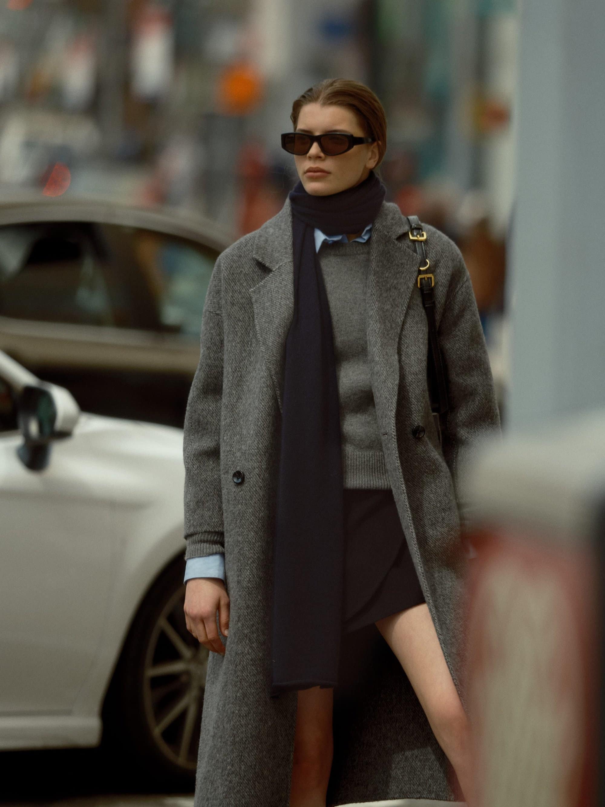 Model in grey wool coat and dark scarf walking on New York City street