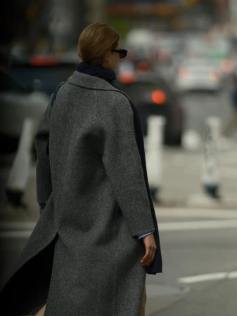 Model seen from behind wearing a grey wool coat walking outdoors on a city street.
