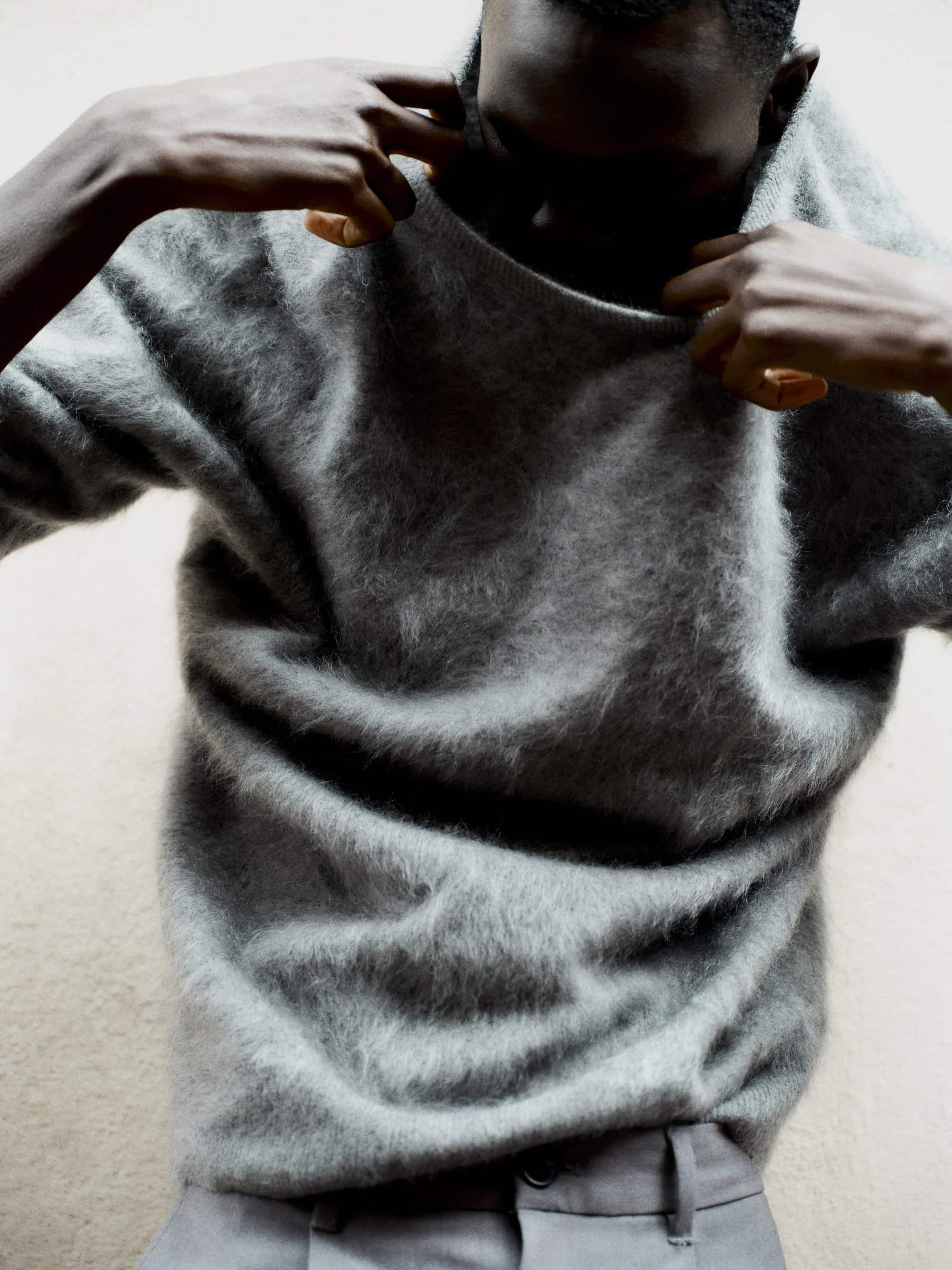 Man adjusting a fuzzy grey sweater against a neutral background for the Soft Goat fall campaign