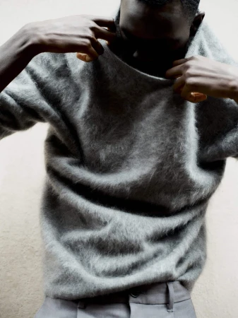 Man adjusting a fuzzy grey sweater against a neutral background for the Soft Goat fall campaign