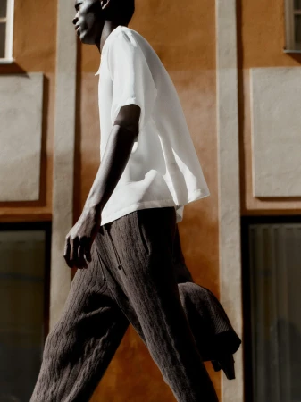 Low angle side profile of a black man wearing a white short sleeve shirt walking past an ochre wall