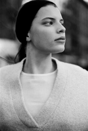 Monochrome portrait of a woman wearing a textured knit cardigan and looking away against an urban street background.