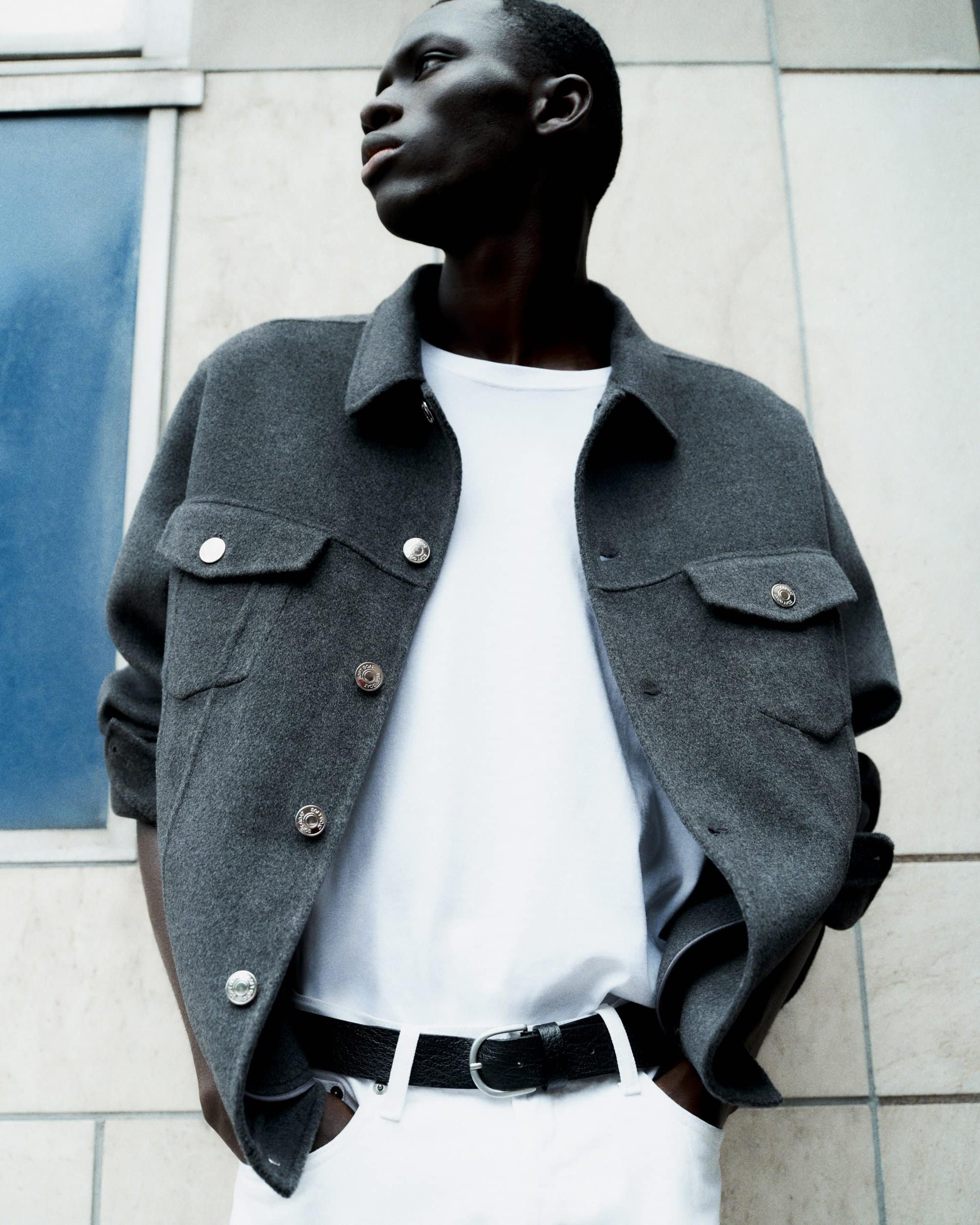 Black man wearing dark grey wool jacket and white t-shirt against building exterior