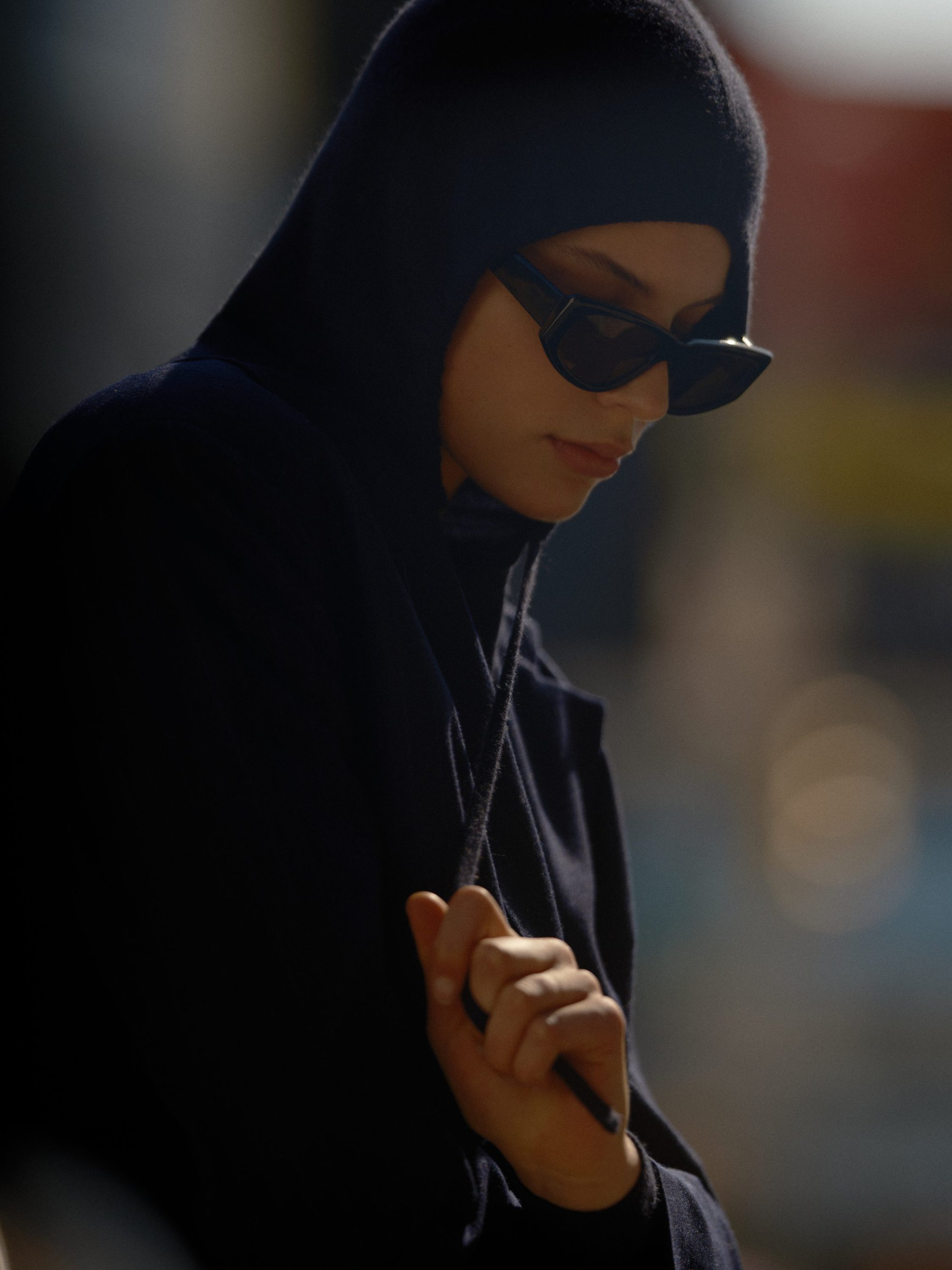 Model wearing a dark hooded top and sunglasses outdoors against a blurred background for Soft Goat.