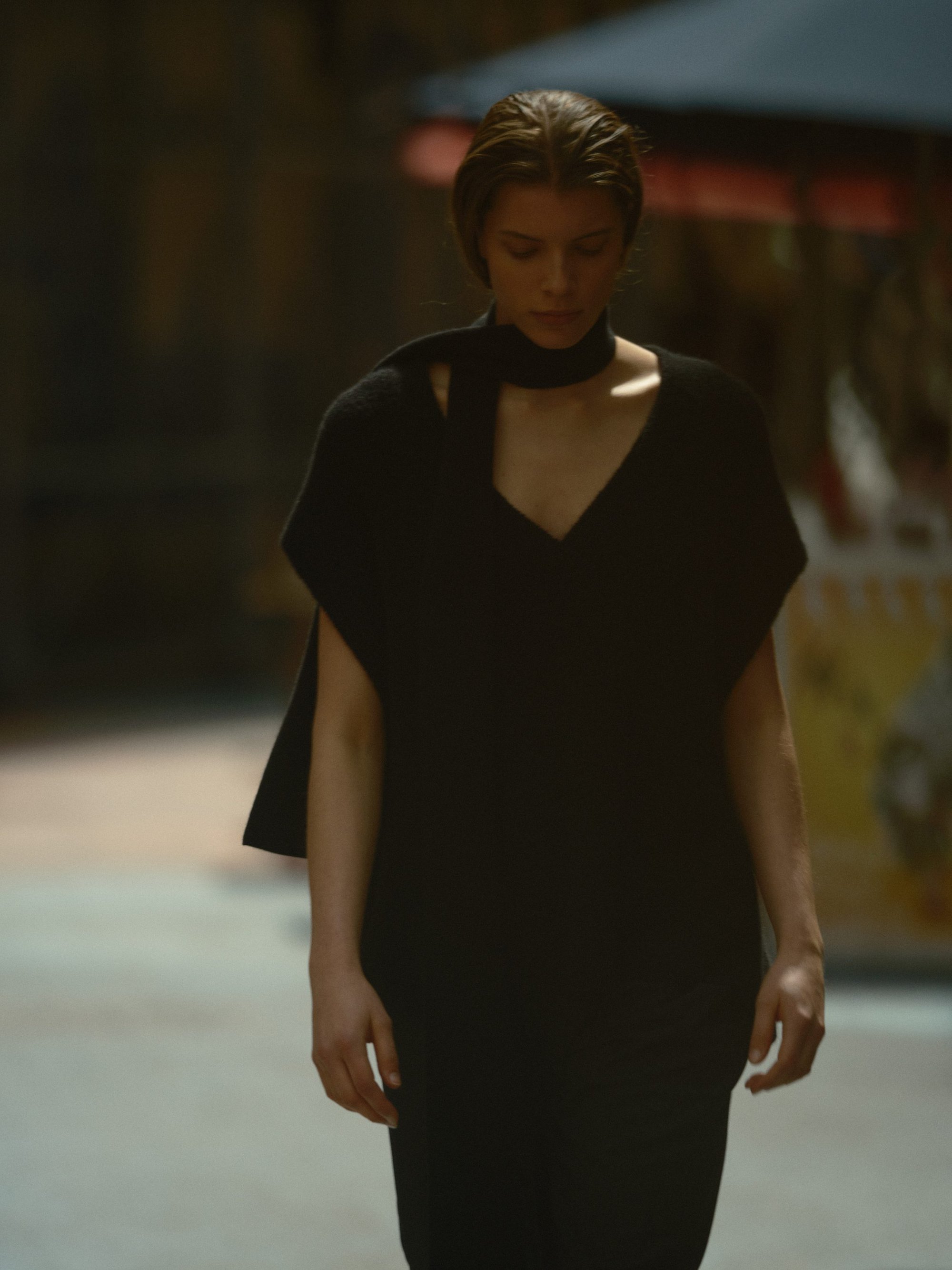 Model in a black knit top with a matching scarf standing outdoors on an urban street.