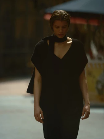 Model in a black knit top with a matching scarf standing outdoors on an urban street.