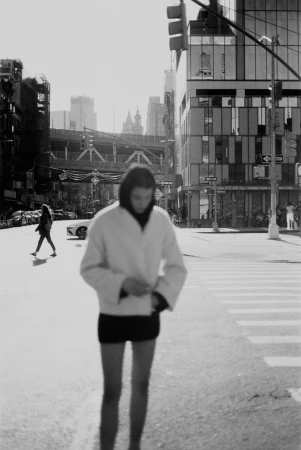 Monochrome street scene in New York featuring a person standing in a light jacket and shorts with city buildings in the background.