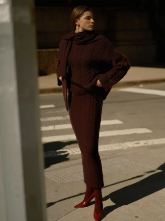 Model wearing a matching burgundy knit sweater and long skirt standing on an urban street.