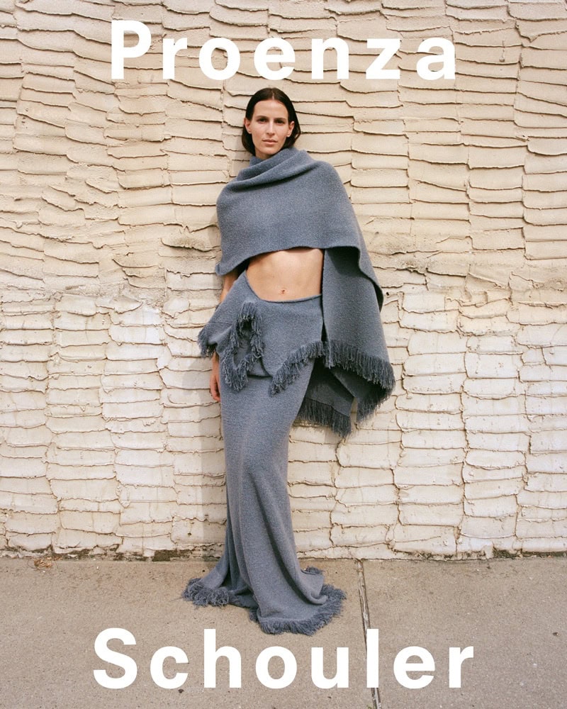 Model in grey fringe knit top and matching skirt standing against a textured wall for Proenza Schouler Fall 2024 ad campaign.