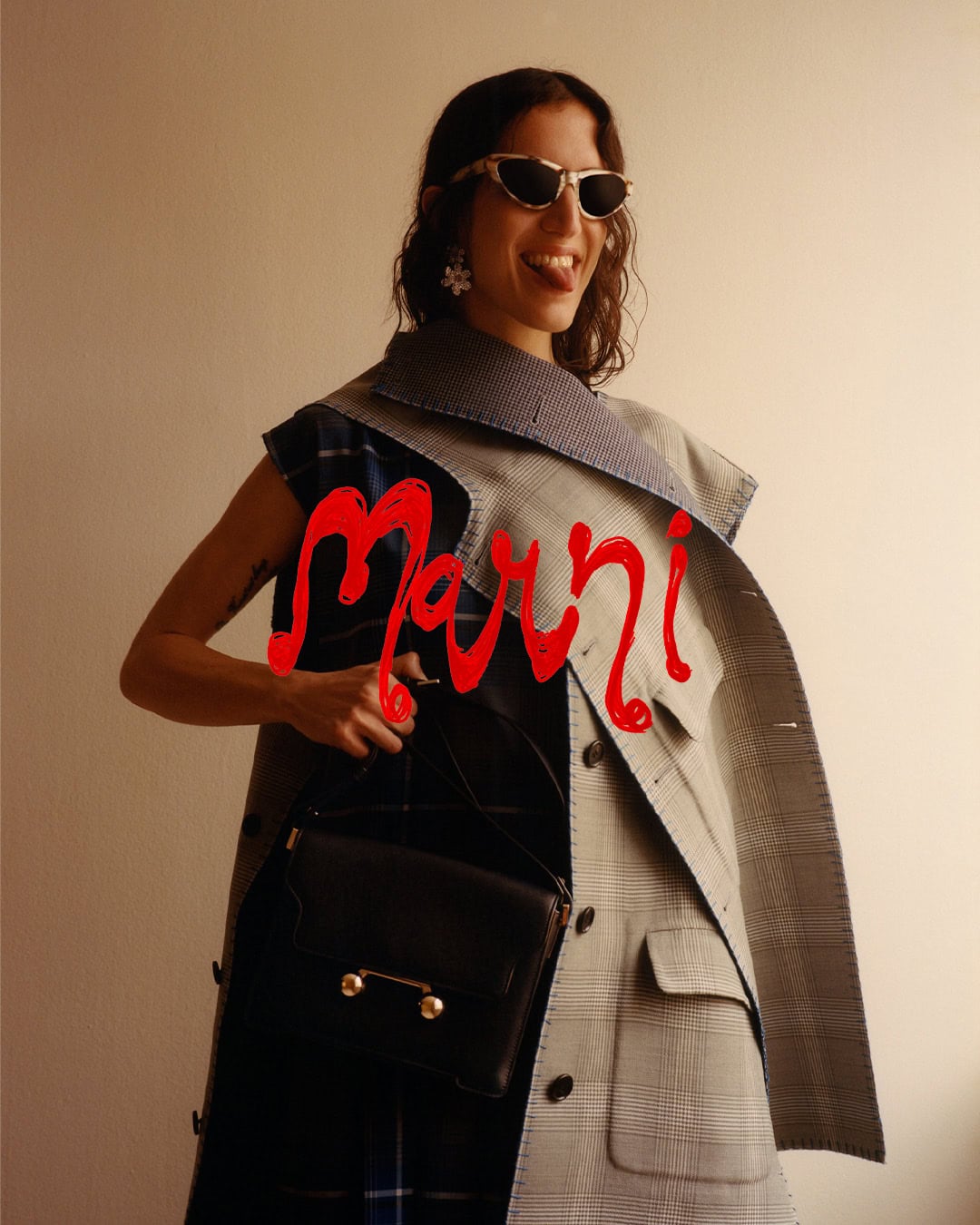Model wearing sunglasses and a patterned vest holding a black handbag for Marni Fall 2024 Vol. 1 Ad Campaign