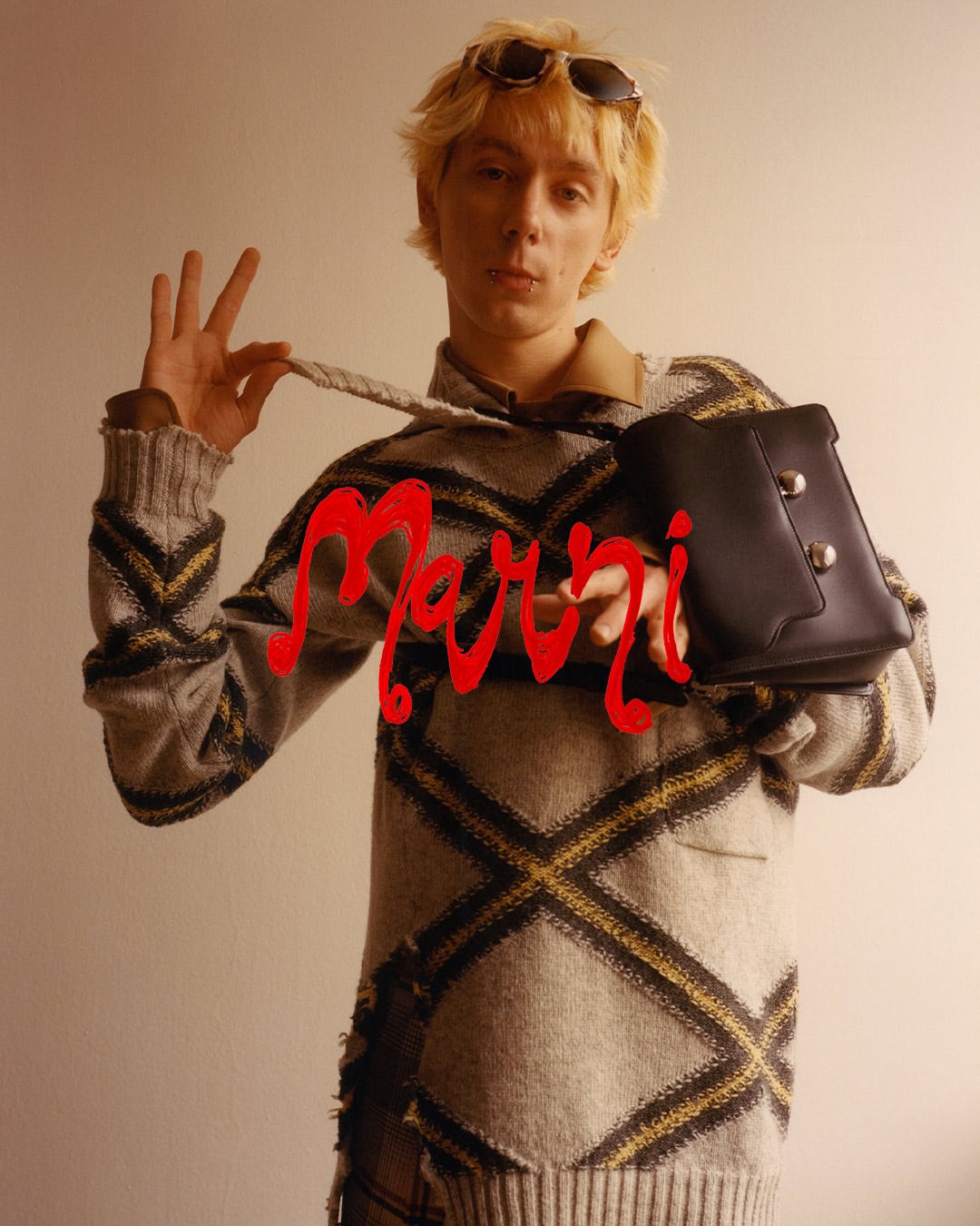 Blonde model wearing a patterned sweater and holding a black handbag for Marni Fall 2024 Vol. 1 ad campaign.