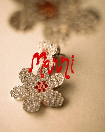 Close-up of a rhinestone flower earring with red center stones, featuring the red Marni brand logo script across the frame.
