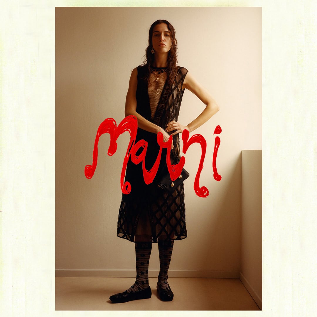 Model wearing a sheer black patterned dress and dark socks posing indoors against a plain wall for Marni