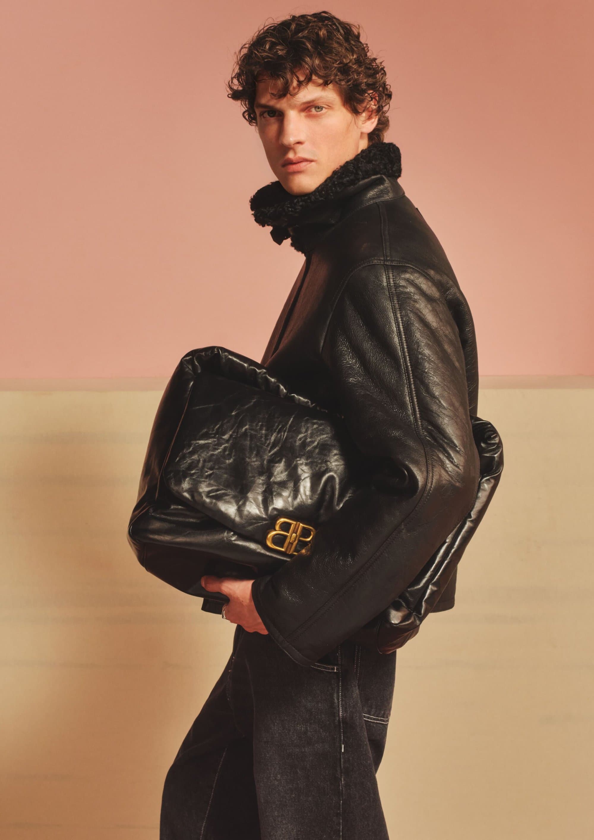 Male model in a black leather jacket holding a large black puffy bag for Mr Porter Fall 2024 campaign