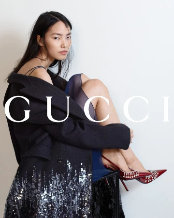 Model wearing dark coat with embellished hem and red heels seated against plain white background