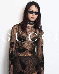 Model in dark sunglasses and sheer black lace top against a white background for Gucci Fall 2024 campaign