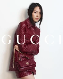 Model in embossed burgundy leather jacket holding matching handbag against plain white studio backdrop