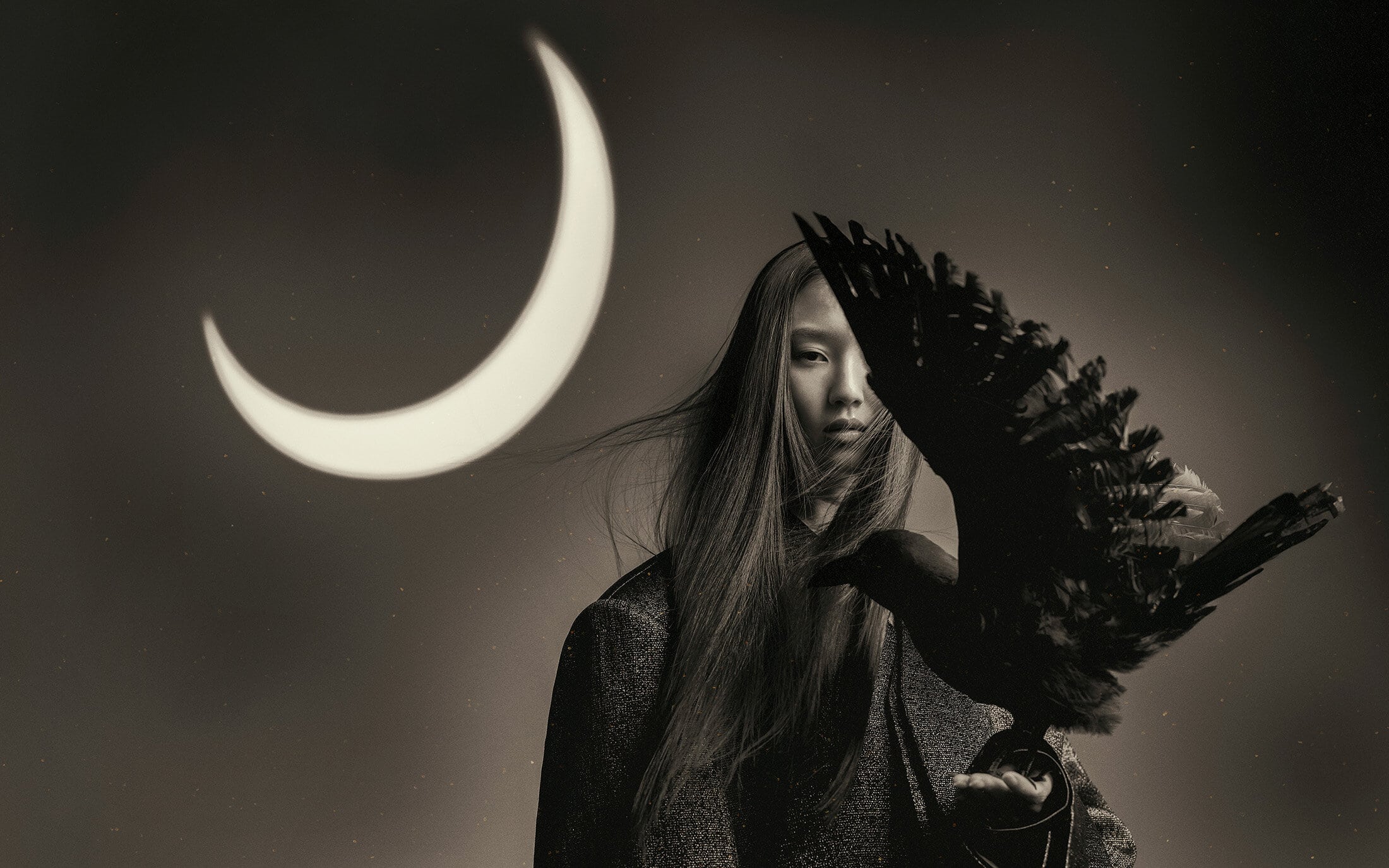 Model holding a large dark bird with a glowing crescent moon in the background