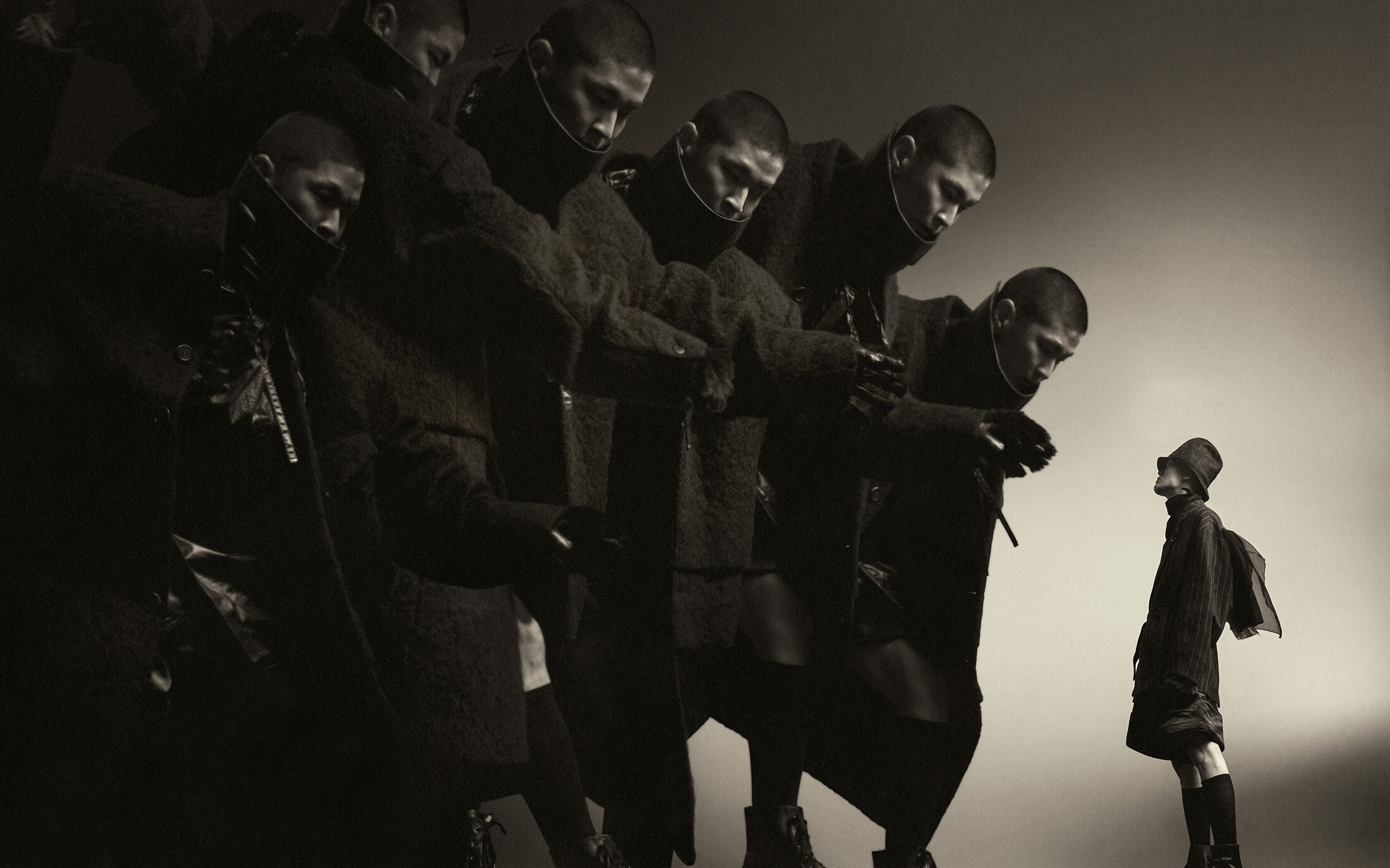 Multiple overlapping figures of a male model in a dark coat beside a smaller figure in the background