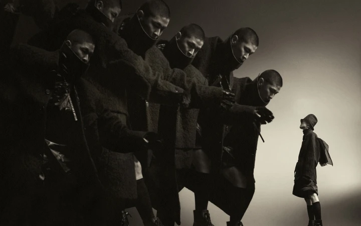 Multiple overlapping figures of a male model in a dark coat beside a smaller figure in the background