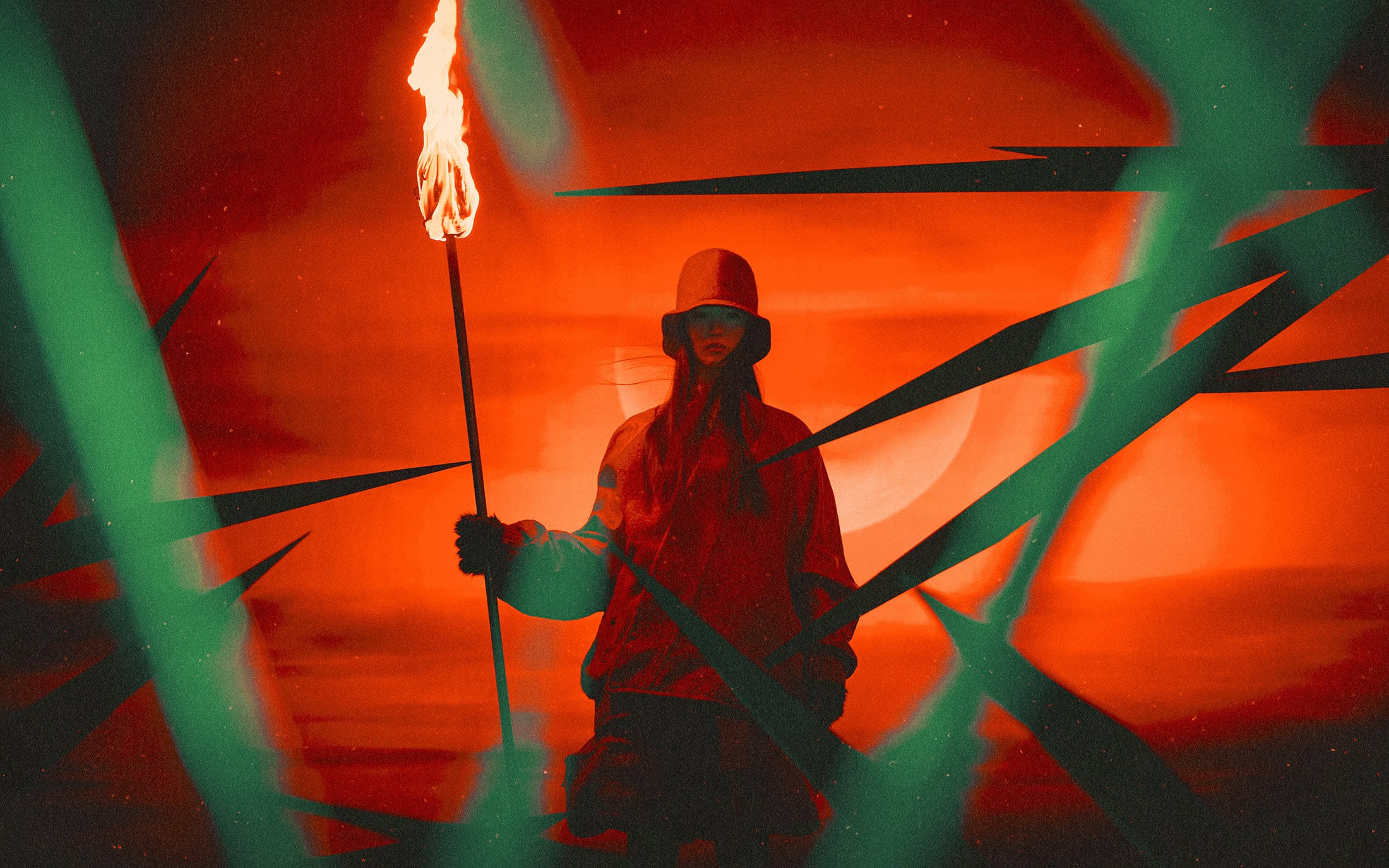 Model wearing a bucket hat and holding a burning torch against a vibrant red background with abstract green light streaks