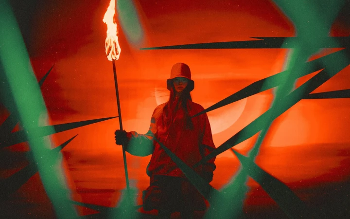 Model wearing a bucket hat and holding a burning torch against a vibrant red background with abstract green light streaks