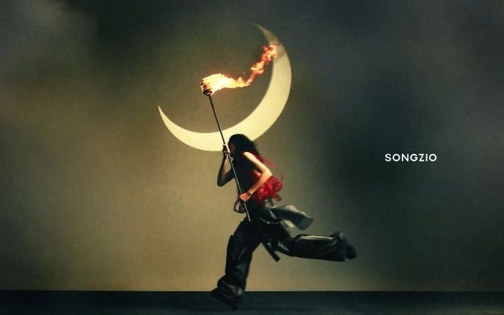 Model running across a dark stage holding a flaming torch beneath a large crescent moon prop for Songzio ad campaign.