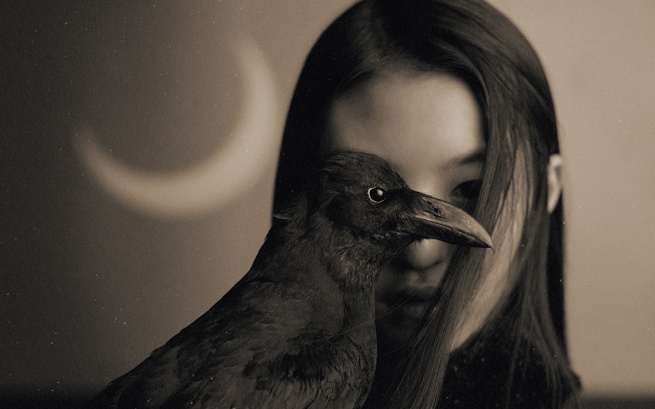 Close-up portrait of a person with long dark hair partially obscured by a dark crow, with a crescent moon in the background.
