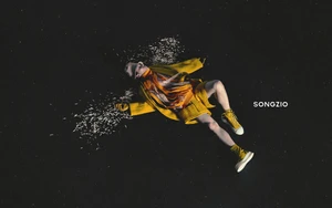 Model lying on a dark textured background wearing a vibrant yellow coat and matching yellow high-top sneakers surrounded by scattered petals.