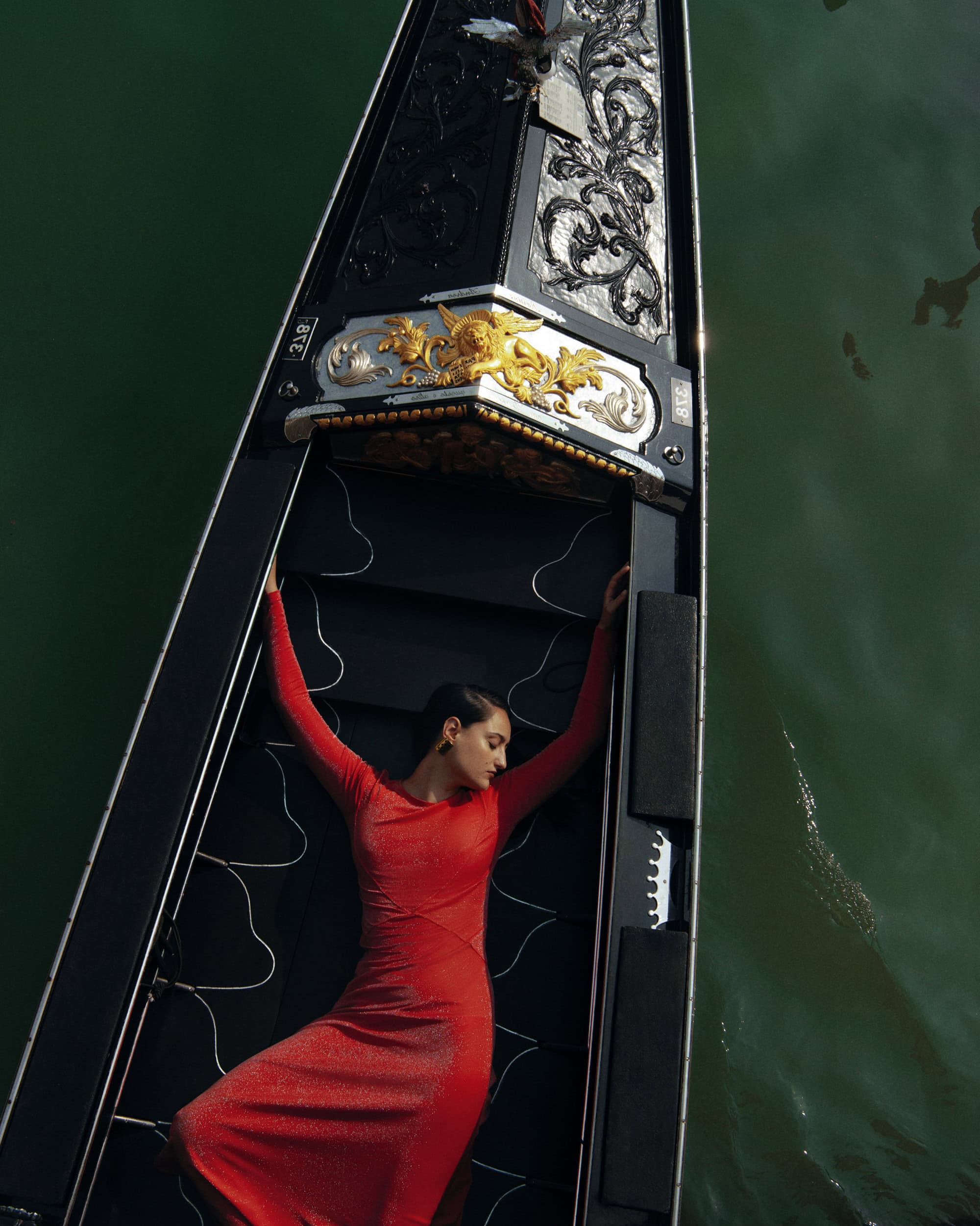 Model in a red dress lying inside a black gondola on the water in Venice
