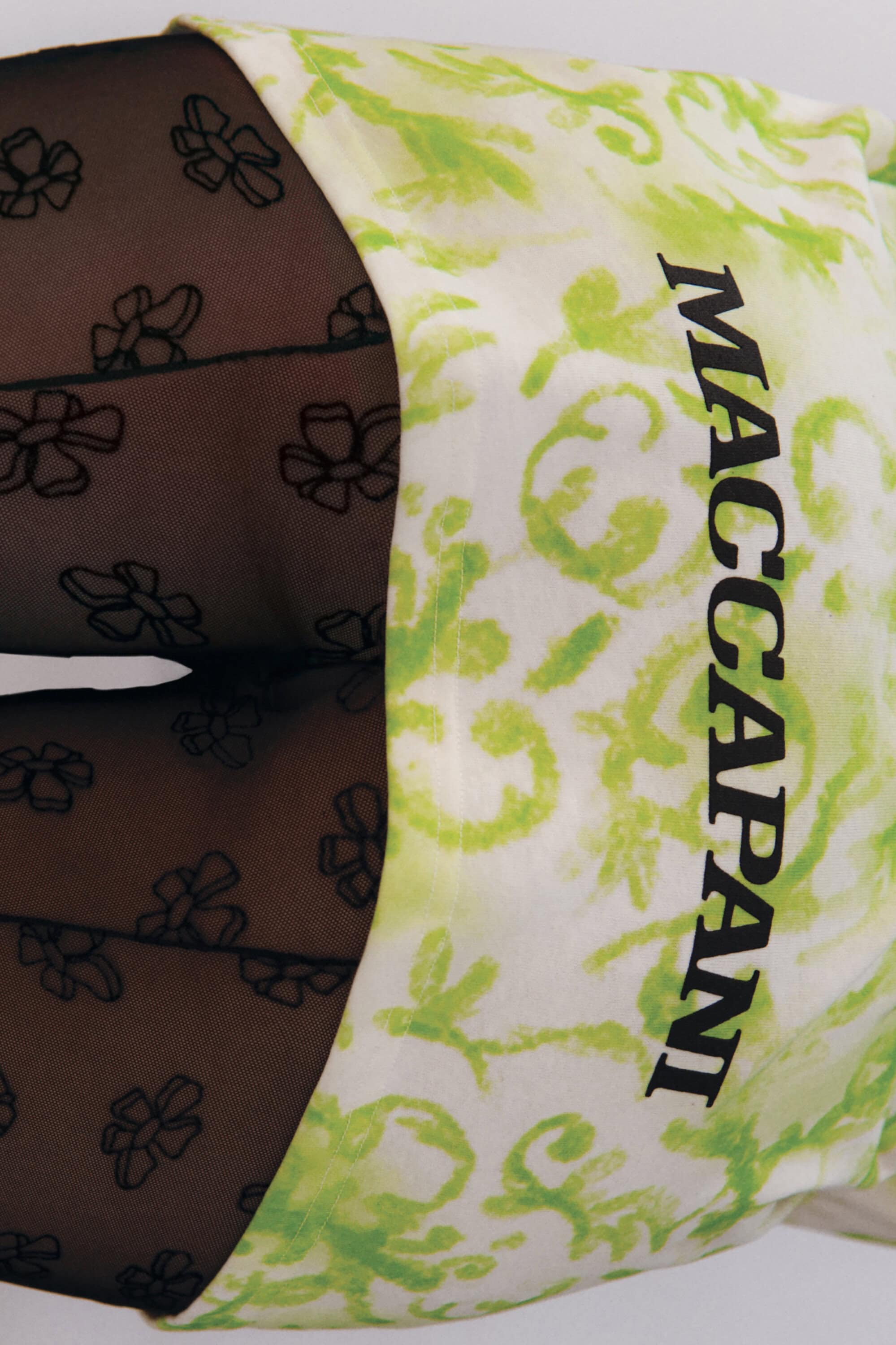 Close-up view of a model wearing a green and white patterned garment and black patterned stockings with a visible Maccapani logo.