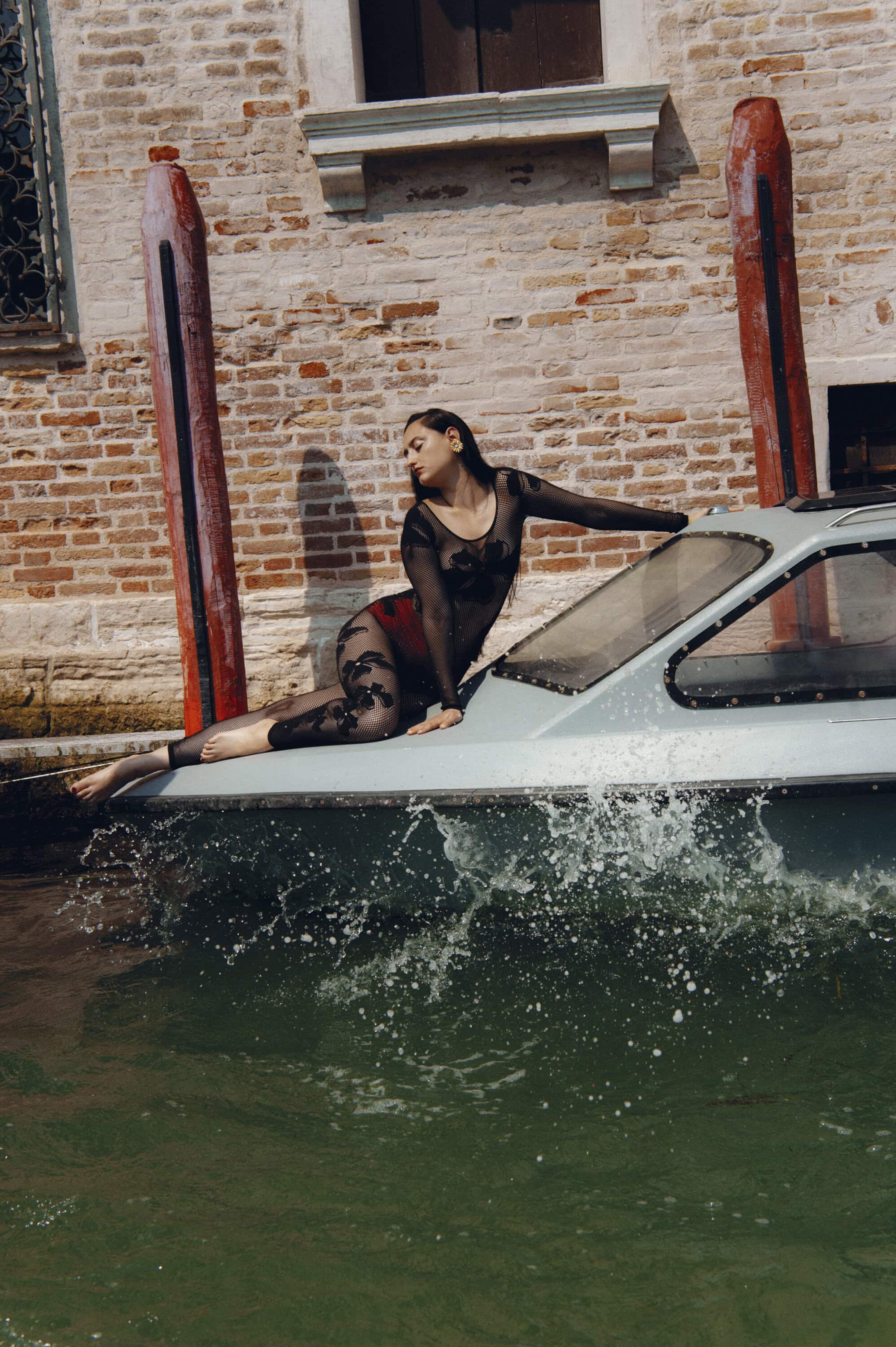 Model posing on the bow of a boat in water with a brick wall background for Maccapani Fall 2024 campaign
