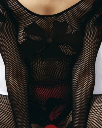 Close-up of a person wearing a long-sleeved black fishnet bodysuit with floral appliqué patterns over red undergarments.