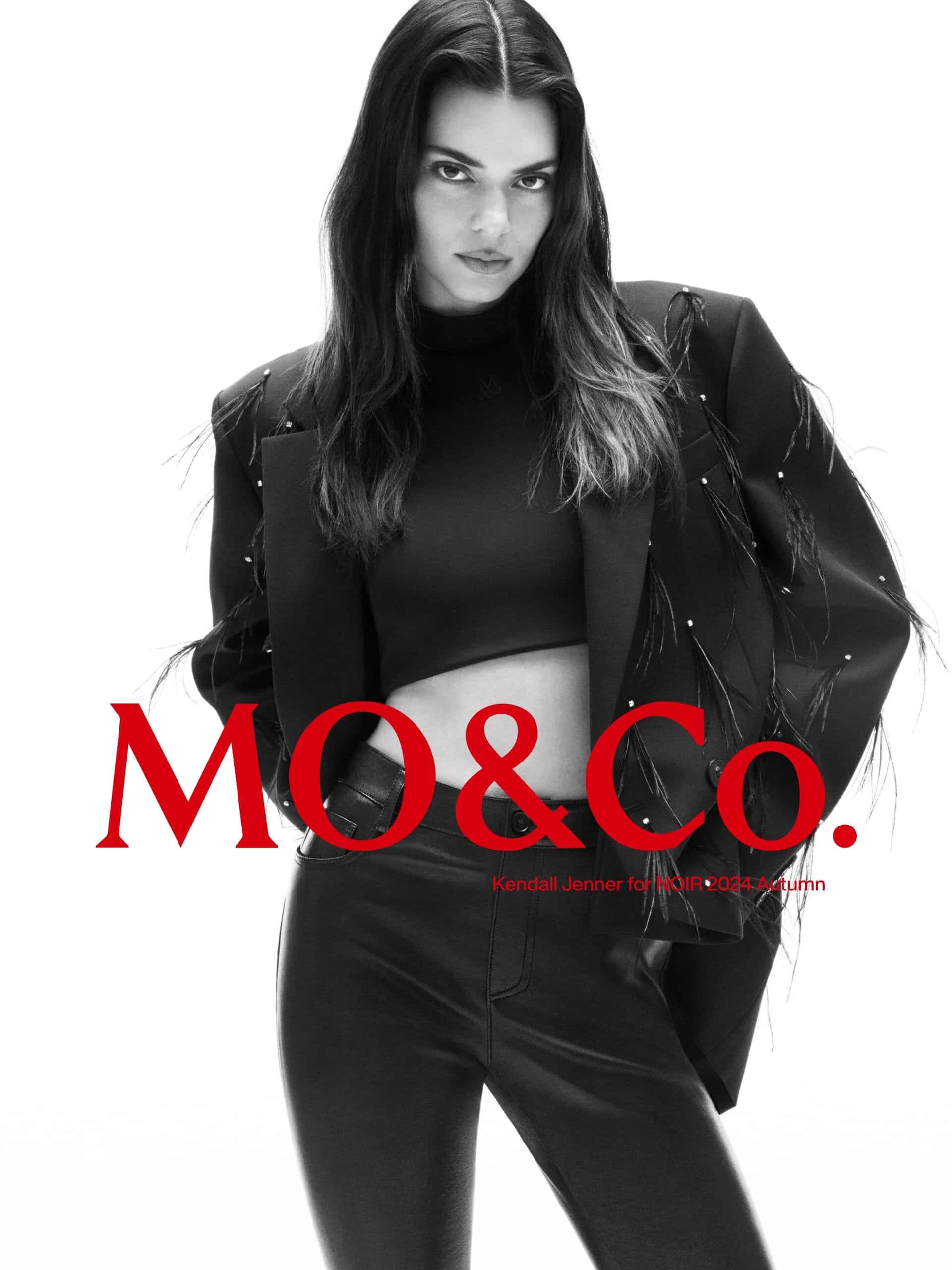 Kendall Jenner in a black blazer and leather trousers for mo.co NOIR 2024 campaign against a white backdrop.