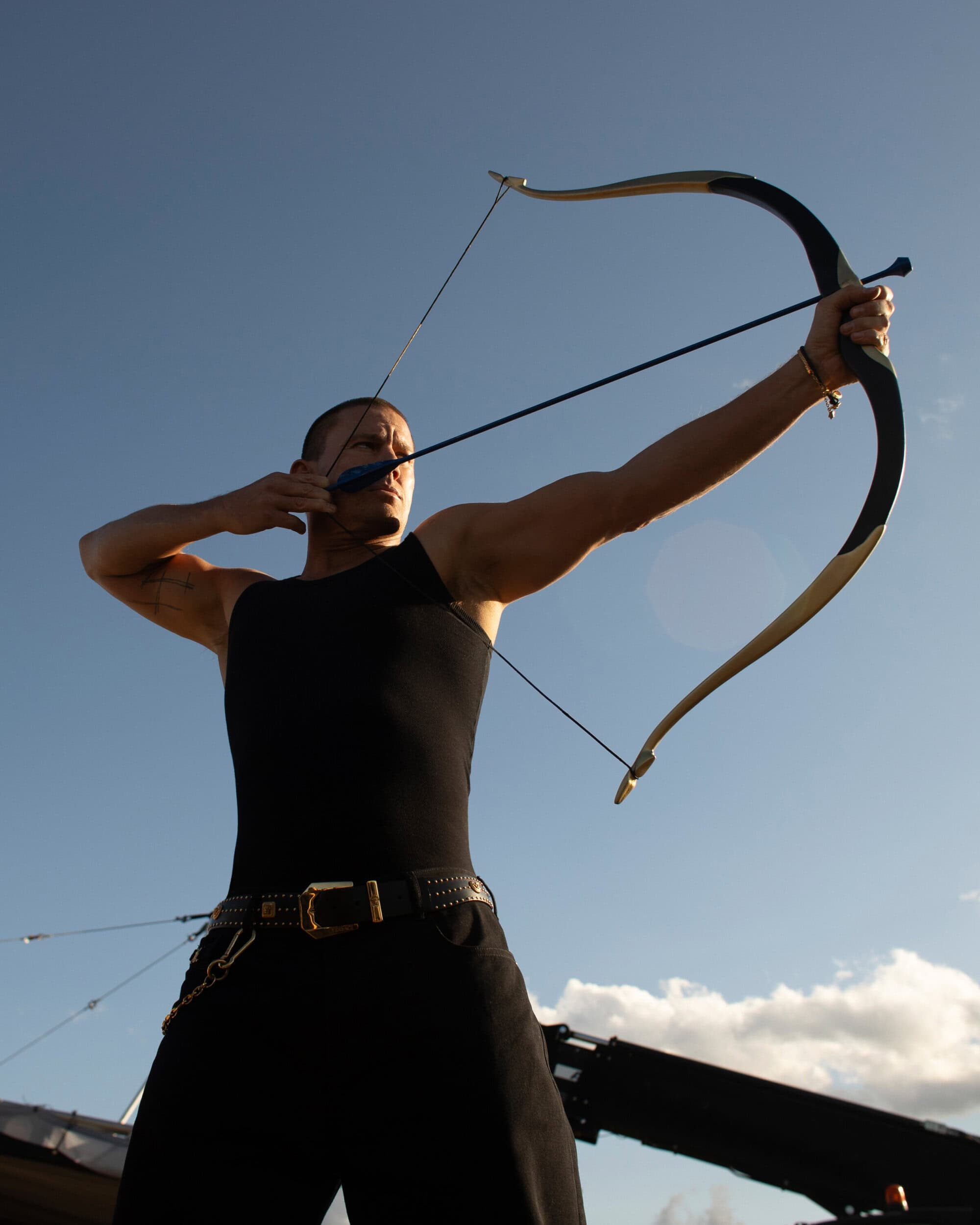Channing Tatum pulling a recurve bow against a clear blue sky for Versace Eros Energy campaign