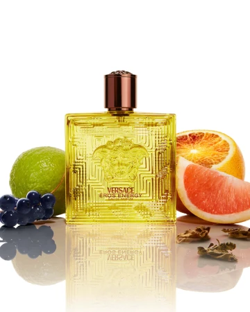 Versace Eros Energy perfume bottle flanked by fresh citrus fruits and dark grapes against a clean white background