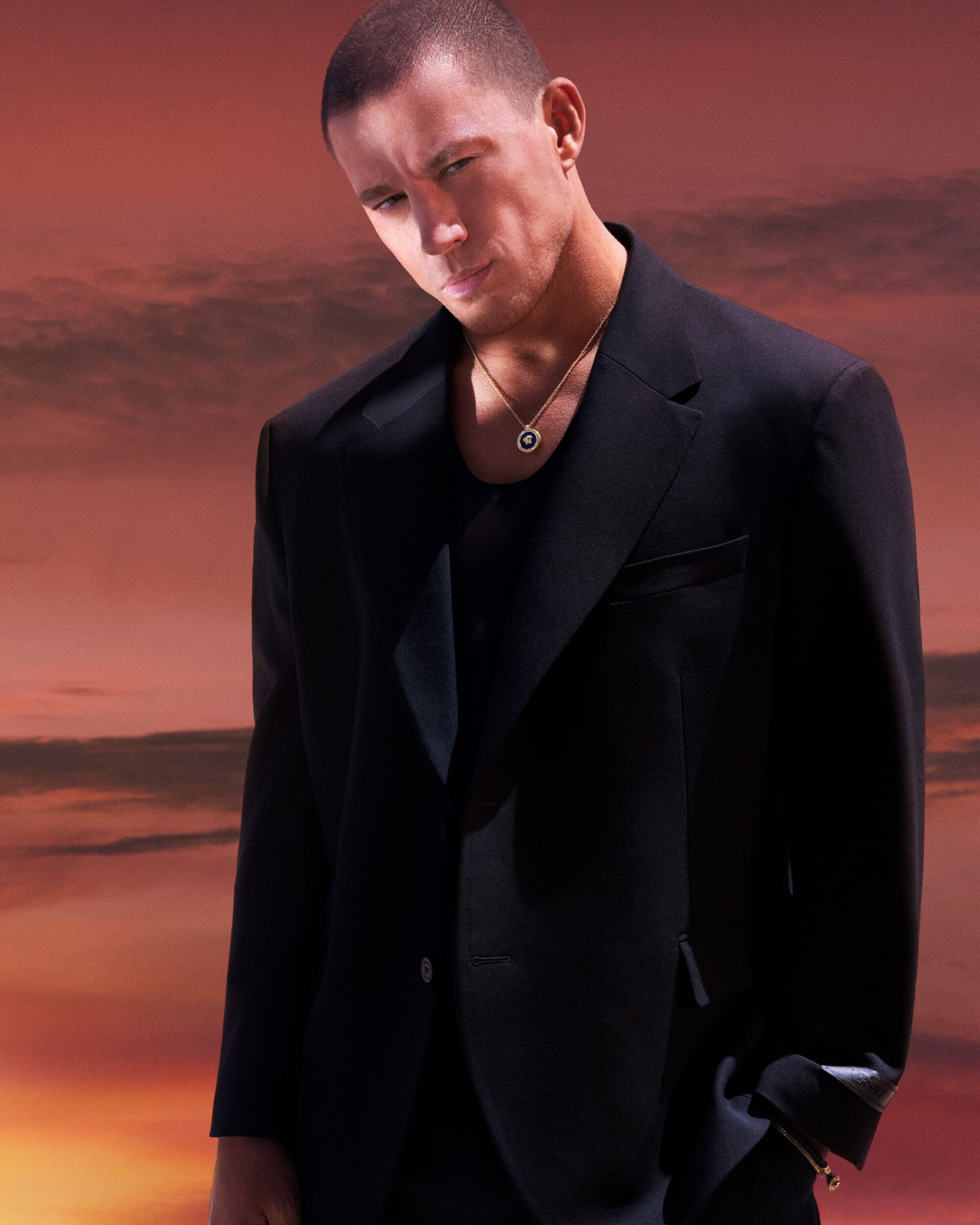 Channing Tatum wearing a black blazer and gold necklace against a sunset sky for Versace Eros Energy campaign