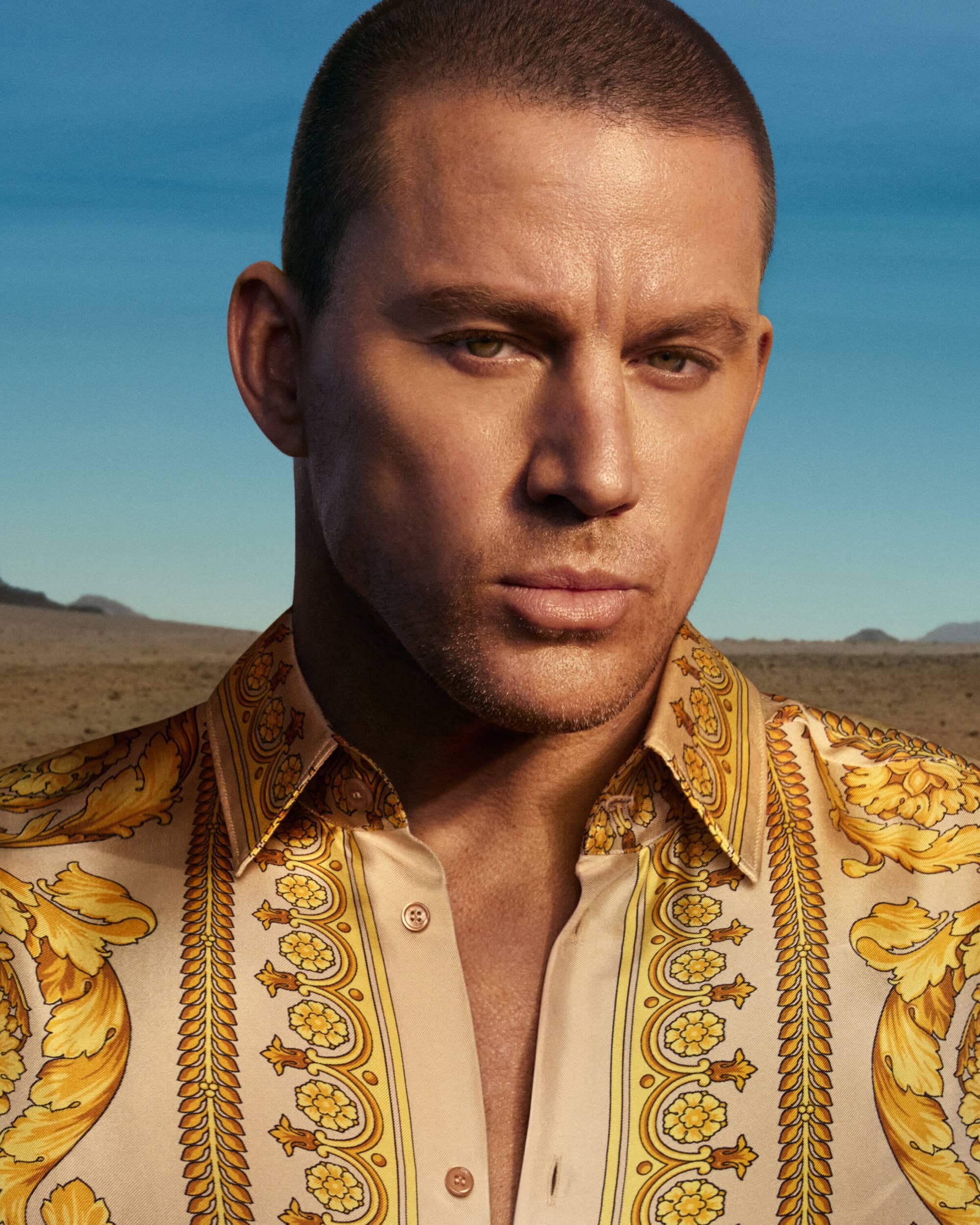 Channing Tatum wearing a patterned silk shirt against a desert and clear blue sky background for Versace.