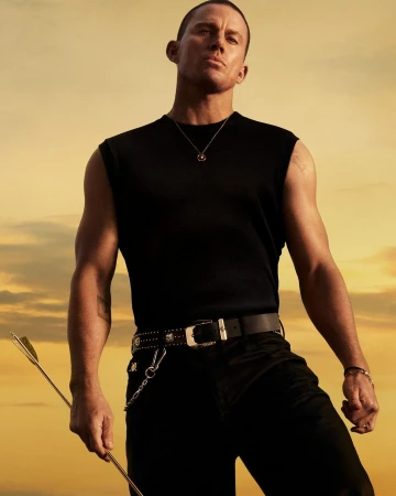 Channing Tatum wearing a black sleeveless top and black jeans against a warm sunset sky holding an arrow