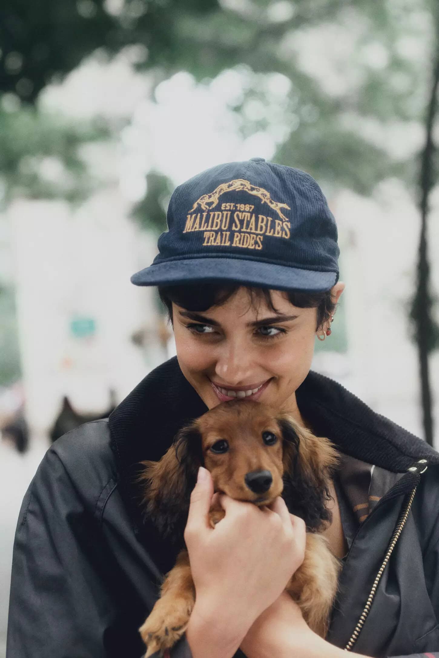 Woman wearing a dark blue cap holding a long-haired dachshund puppy outdoors in New York City.