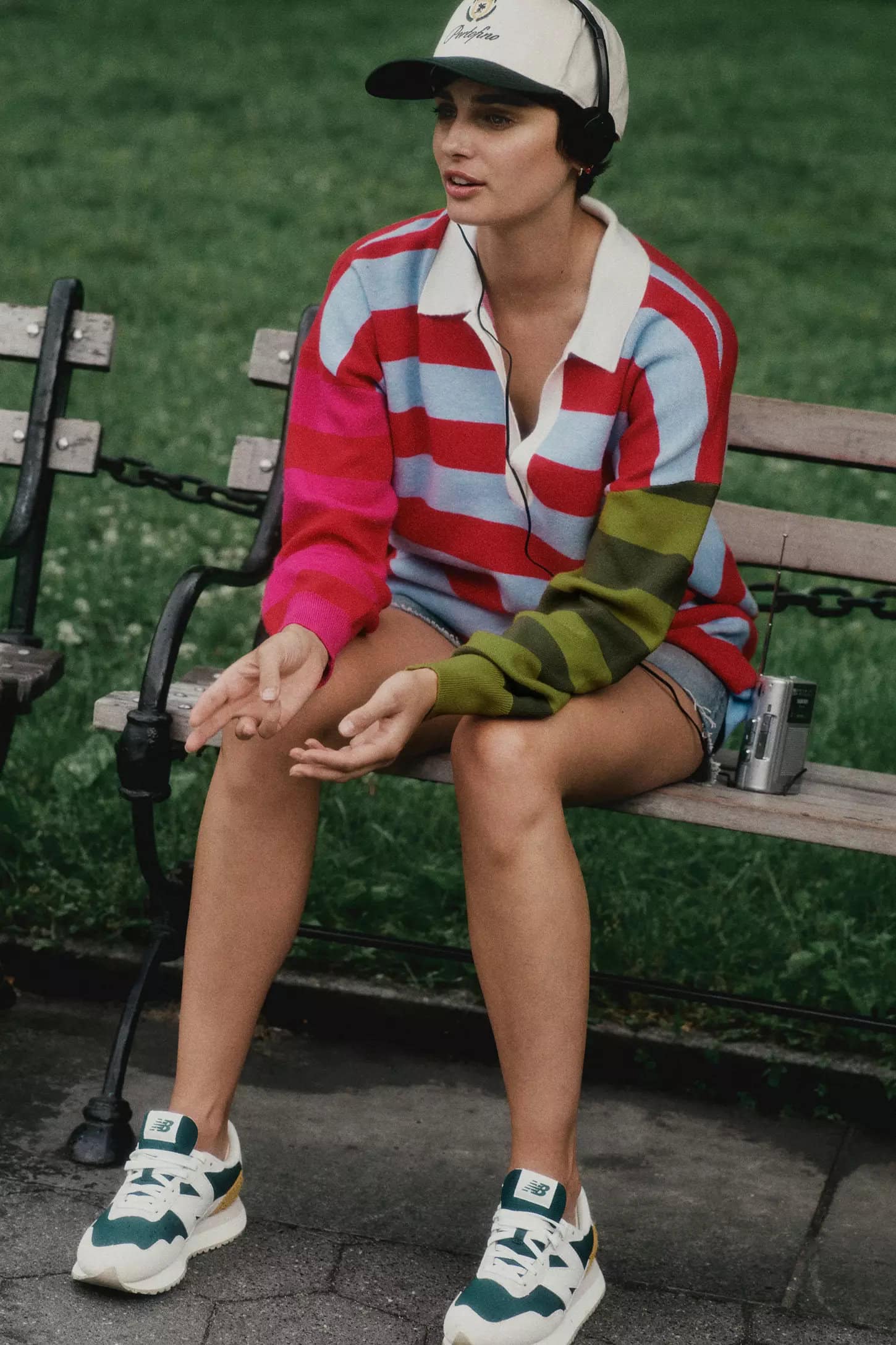 Woman wearing a multi-coloured striped polo sweater and baseball cap seated on a park bench