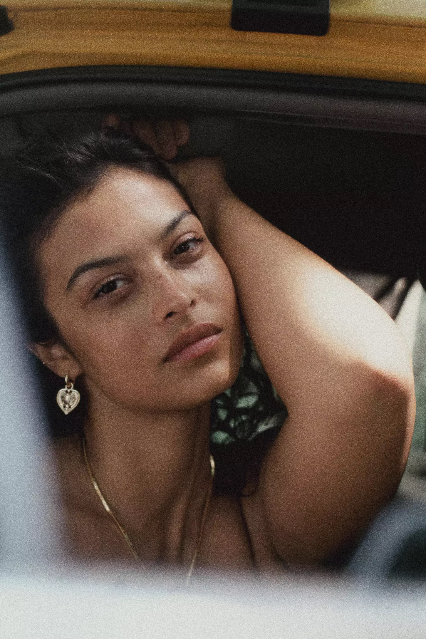 Portrait of a woman resting inside a vehicle, wearing a heart pendant earring and gold chain necklace, shot for Anthropologie.
