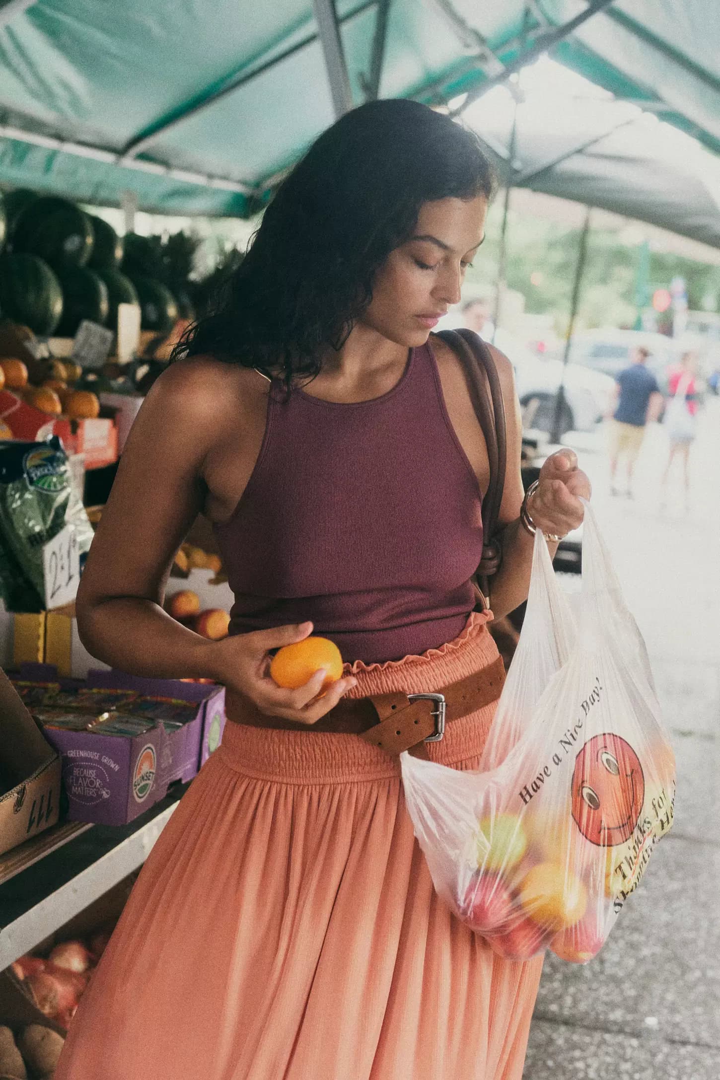 Woman holding an orange and a plastic produce bag while shopping at an outdoor market stall