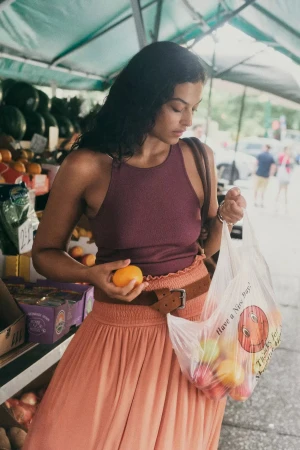 Woman holding an orange and a plastic produce bag while shopping at an outdoor market stall