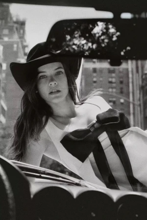 Model wearing a wide-brimmed hat leaning against a car in New York City for the Anthropologie Fall 2024 campaign.