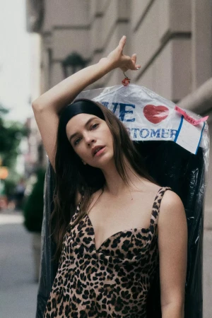 Model Barbara Palvin wearing a leopard print dress and headband holding a garment bag outdoors on a New York City street.